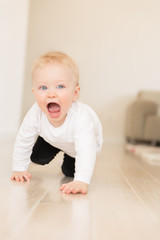 Nicely dressed and happy baby girl with blue eyes crawling on the ground.