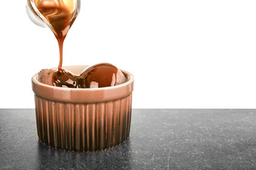 Pouring caramel sauce onto chocolate ice cream in bowl against white background
