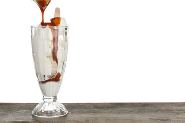 Pouring caramel sauce onto vanilla ice cream in dessert glass against white background