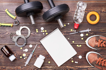 Paper notebook, syringe, dumbbells, handcuffs. Illegal pills in sport activity.