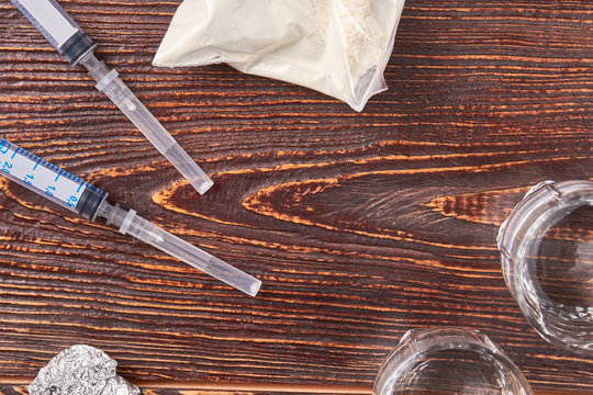 Syringes, heroin, foil, vessels. Set for preparation of narcotics, wooden background.