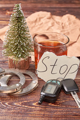 Composition from whiskey, keys and handcuffs. Car keys, handcuffs, message stop, glass of alcohol on wooden background.