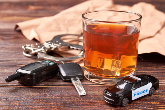 Whiskey, keys, handcuffs, police car. Car key on the bar with spilled alcohol. Alcohol beverage and judgment of police.