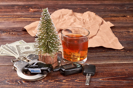 Keys, handcuffs, alcohol, new year tree. Police car in handcuffs, driving keys, whiskey, american money on wooden background.