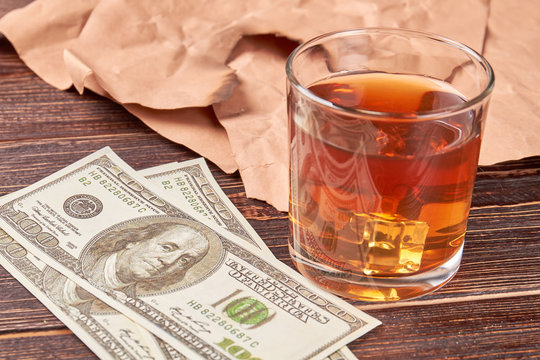 Dollars, glass of whiskey, paper, wooden background. Still life money and alcohol.