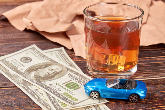 Money and whiskey on wooden background. Dollars, car, glass of alcohol close up. The concept of drink and driving.