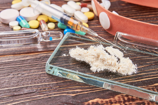 Drugs overdose leads to death. White powder on glass. Syringe, pills, wooden background.