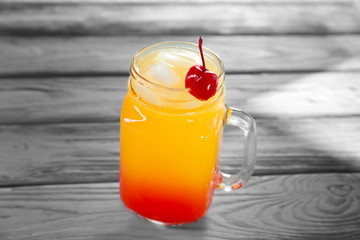 Mason jar of delicious tequila sunrise cocktail on table