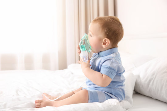 Cute little baby with nebulizer sitting on bed at home. Health care concept