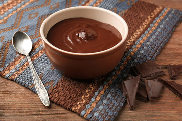 Bowl with delicious melted chocolate and spoon on wooden table