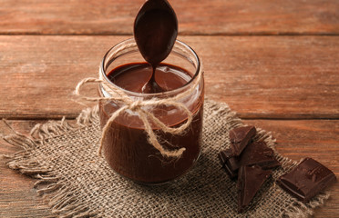 Jar with delicious chocolate sauce on wooden background