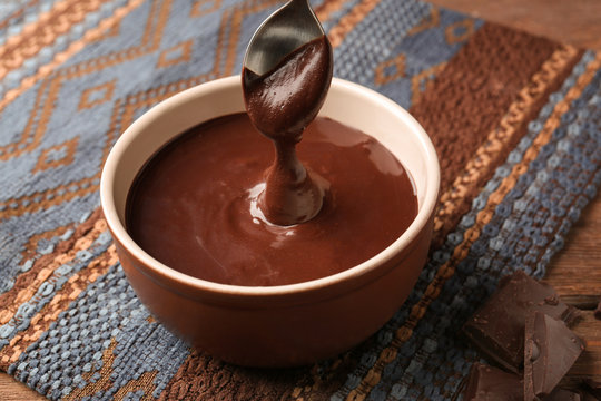 Bowl with delicious melted chocolate sauce and spoon on table