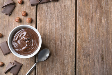 Bowl with delicious chocolate sauce, spoon and nuts on wooden table