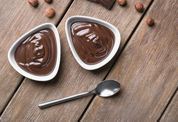 Bowls with delicious chocolate sauce and nuts on wooden table