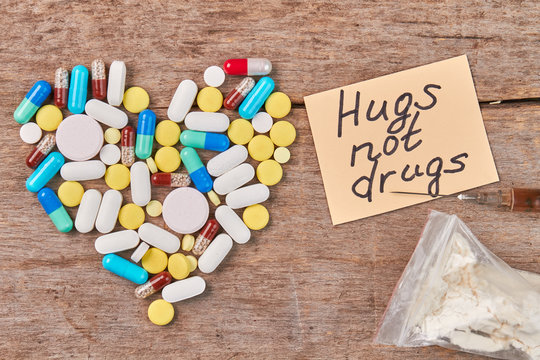 Message hugs not drugs. Heart from colorful pills, note, narcotics, wooden table.