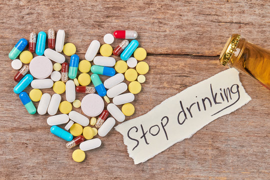 Stop drinking and start new life. Pills shaped heart, message, bottle neck, wooden table.