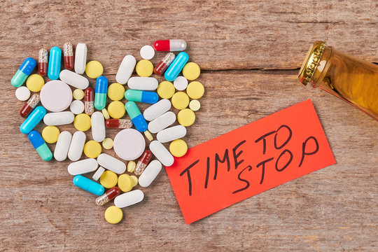 Time to stop drinking alcohol. Heart from colorful pills, message, bottle with alcohol, wooden background.