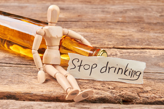 Stop drinking message, wooden dummy. Wooden puppet, transparent bottle, wooden background.