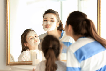 Young woman and her little daughter with facial masks at home