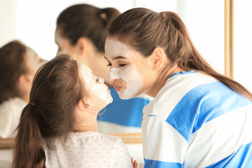 Fototapeta premium Young woman and her little daughter with facial masks at home