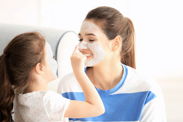 Young woman and her little daughter with facial masks at home