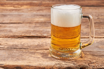 Glass mug with beer and foam. Full transparent glass of beer on old wooden background.