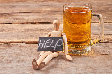 Help to get rid of alcohol. Human wooden figurine with message help, glass of beer, old wooden background.
