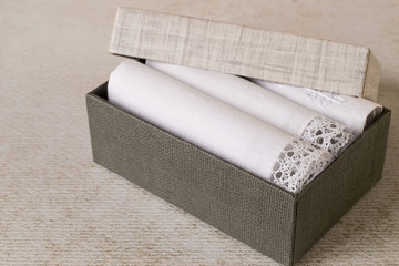  Accessories. A set of white handkerchiefs with decorative trim in a cardboard box on a light background. The idea for a gift. 