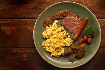 A simple breakfast consists of eggs, ham, bacon and fries.