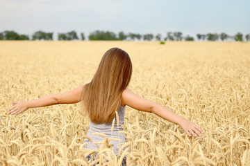 Beautiful girl with long heir walking through golden wheat field. Concept of purity, growth, happiness