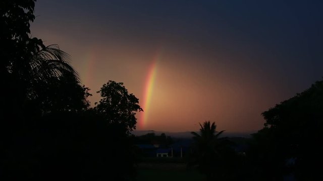 Rainbow in sky evening over residential, trees in Thailand city with dark sunshine in summer