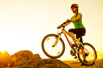 Fototapeta na wymiar Young Woman Riding Mountain Bike on the Summer Rocky Trail at Beautiful Sunset. Travel, Sports and Adventure Concept.