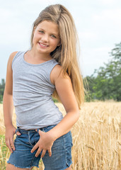 adorable little girl with long heir Posing in golden wheat field at a summer day