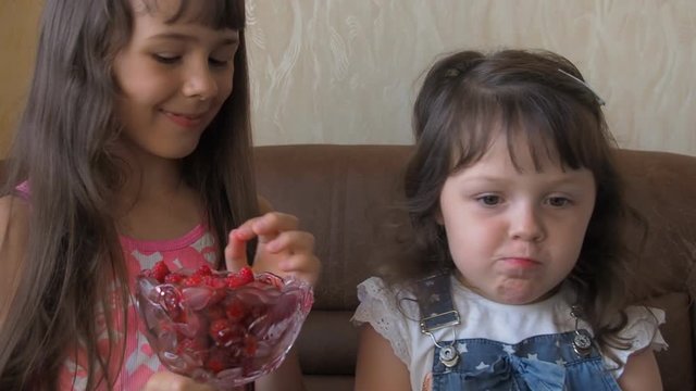 A child eats raspberries. Two sisters feed each other raspberries.