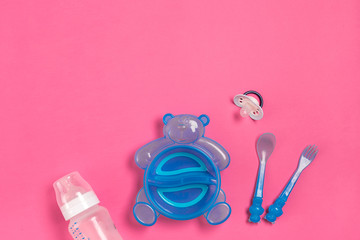 Blue plate in the form of a bear, a bottle, knife and spoon on pink table. Children dinner time. Top view