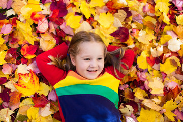 Naklejka na ściany i meble Child in fall park. Kid with autumn leaves.