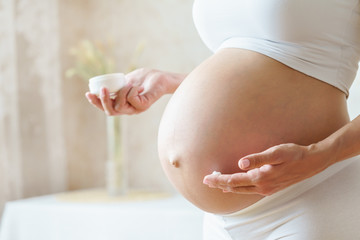 Pregnant woman aplying cream at her belly for prevention of stretch marks on the skin