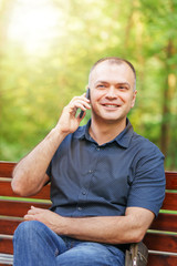 Fototapeta premium adult man around 35-40 is talking with smile by phone at summer park