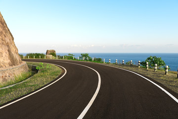 New Asphalt coastal road with white markings going round cliff edge bend, with blue sea and clear...