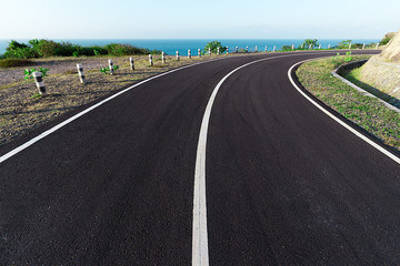 New Asphalt coastal road with white markings going round cliff edge bend, with blue sea and clear sky back drop.