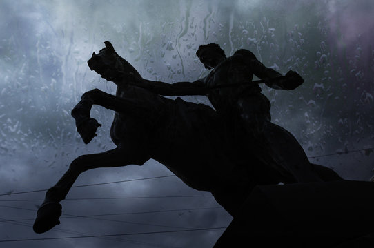 Silhouette of statue the Tamers of horses  on the dark sky background, view through wet window