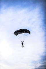 Silhouette of parachuter on a blue sky with clouds on it.