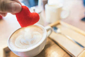 Hands holding a small heart to be put into the coffee in selective focus. Concept : art, love coffee, attention