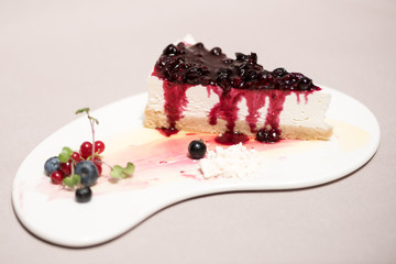 Fancy dessert with cheesecake and forest fruits,  on white plate, light brown background