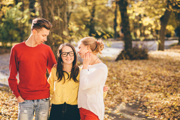 Season, study, education and people concept. Group of three sudents hugging and talking in autumn park.