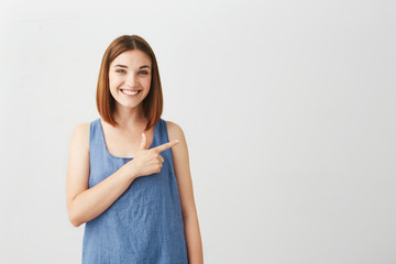 Young beautiful brunette girl smiling looking at camera pointing finger in side over white background.