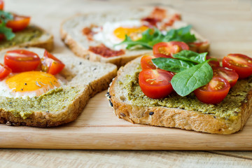 Fototapeta na wymiar Breakfast toasts with multicereal bread, pesto sauce, cherry tomatoes, eggs, spinach on wooden cutting board. Healthy breakfast. Balanced meal