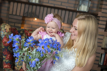 Happy one year old girl with young mother and a bouquet of flowers