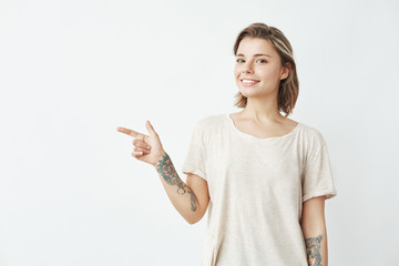 Cheerful young pretty girl smiling looking at camera pointing finger in side over white background.