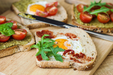 Healthy balanced toasts with egg, arugula, red cherry tomatoes, spinach leaves, pesto and tomato sauce and multicereal bread. Healthy breakfast sandwiches